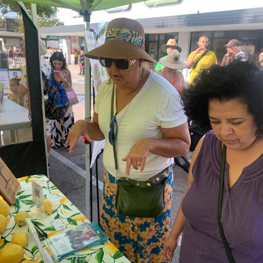 People visiting an informational table with brochures and fresh lemons at an outdoor community event.